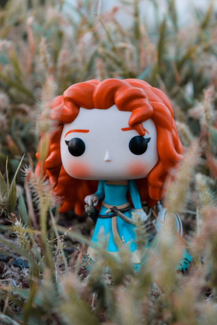 Colorful figurine with red hair in outdoor grass setting, showcasing a whimsical fantasy theme.