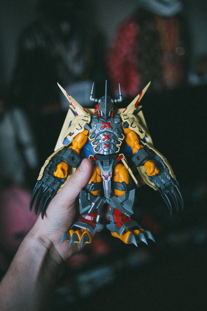 Detailed close-up of a hand holding a Wargreymon toy against a dark background.